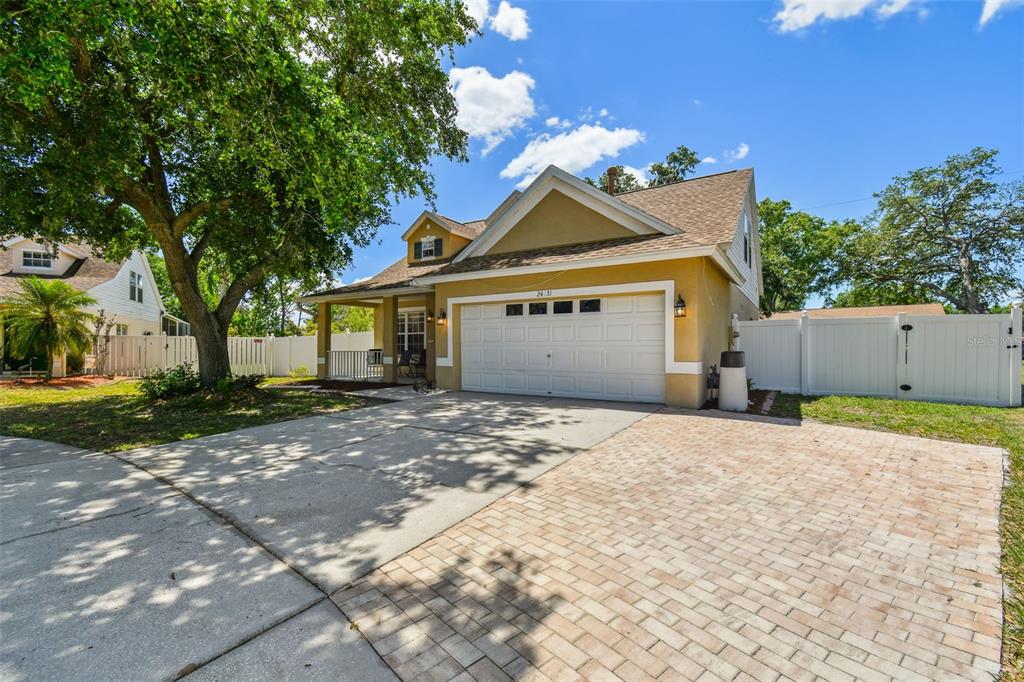 A yellow house with a white garage door, a paved driveway, and a large shade tree — 24231 SATINWOOD COURT, LUTZ, FL