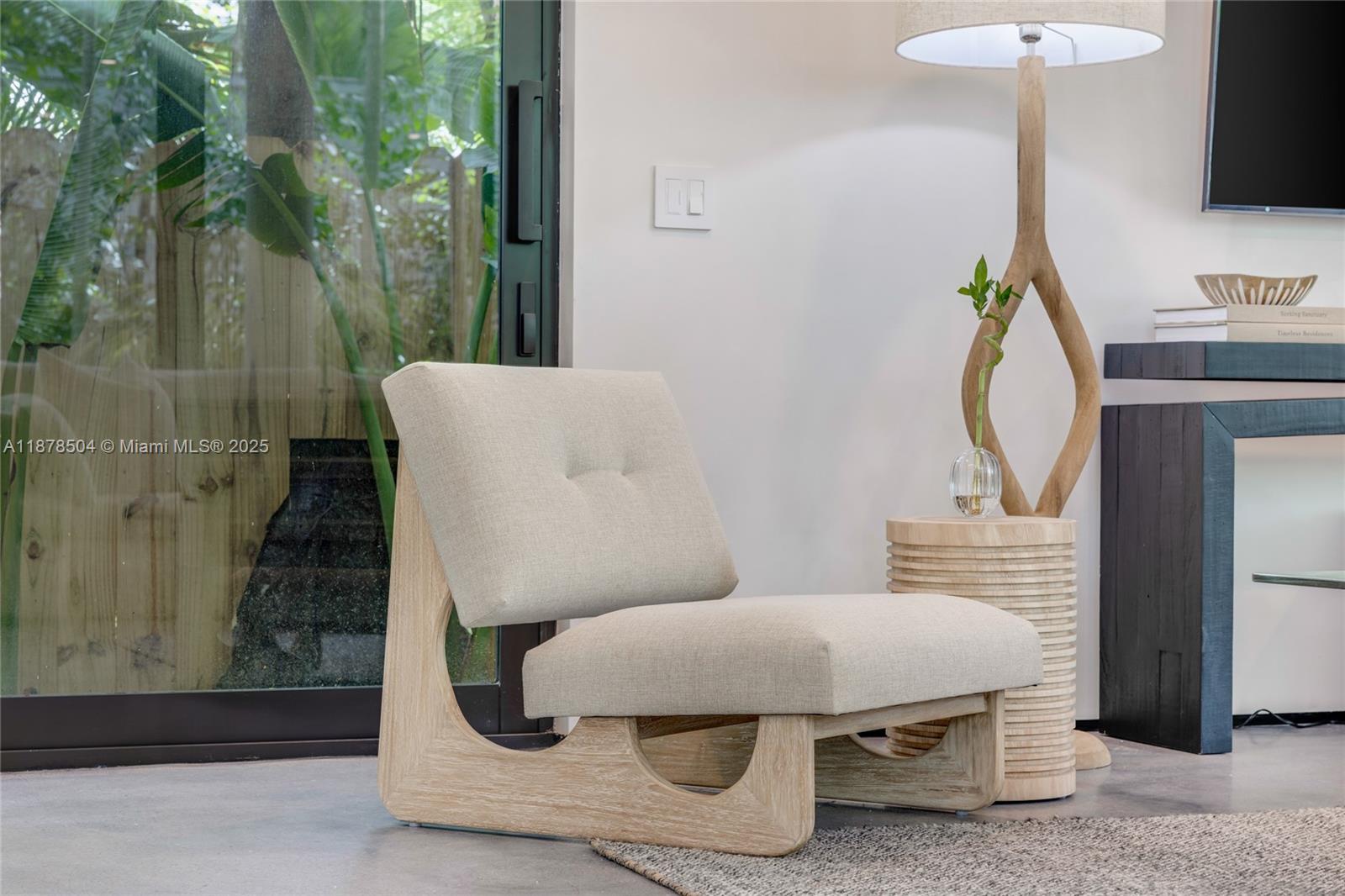 A modern beige upholstered chair sits on a concrete floor next to a wooden lamp — 1000 NW 9th Ct, Miami FL 33136, MIAMI, FL