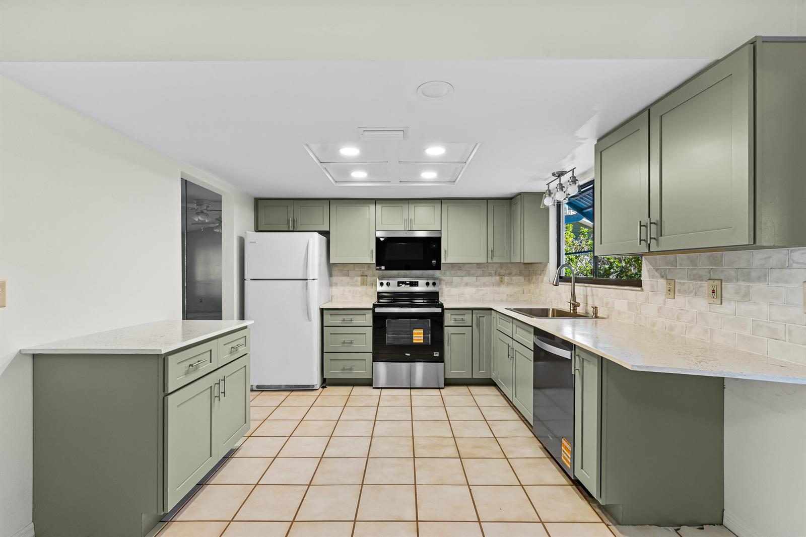 A kitchen features sage green cabinets, stainless steel appliances, white countertops, and light tile flooring — 975 4th Lane, Vero Beach FL 32962, VERO BEACH, FL
