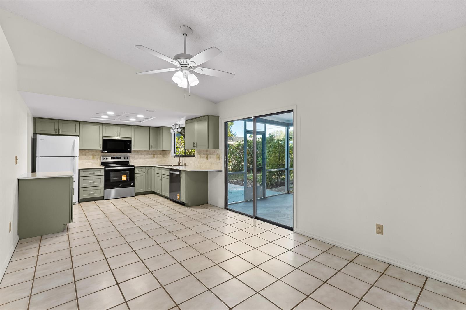 A kitchen with sage green cabinets, tile flooring, and a sliding glass door to a patio — 975 4th Lane, Vero Beach FL 32962, VERO BEACH, FL