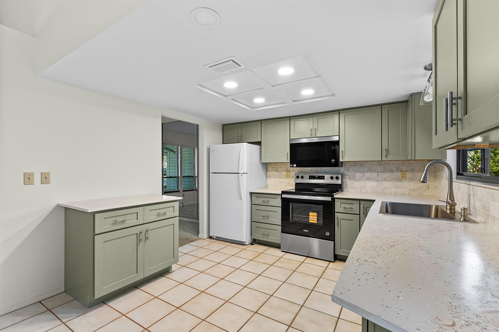 A kitchen features sage green cabinets, light countertops, stainless steel appliances, and beige tile flooring — 975 4th Lane, Vero Beach FL 32962, VERO BEACH, FL
