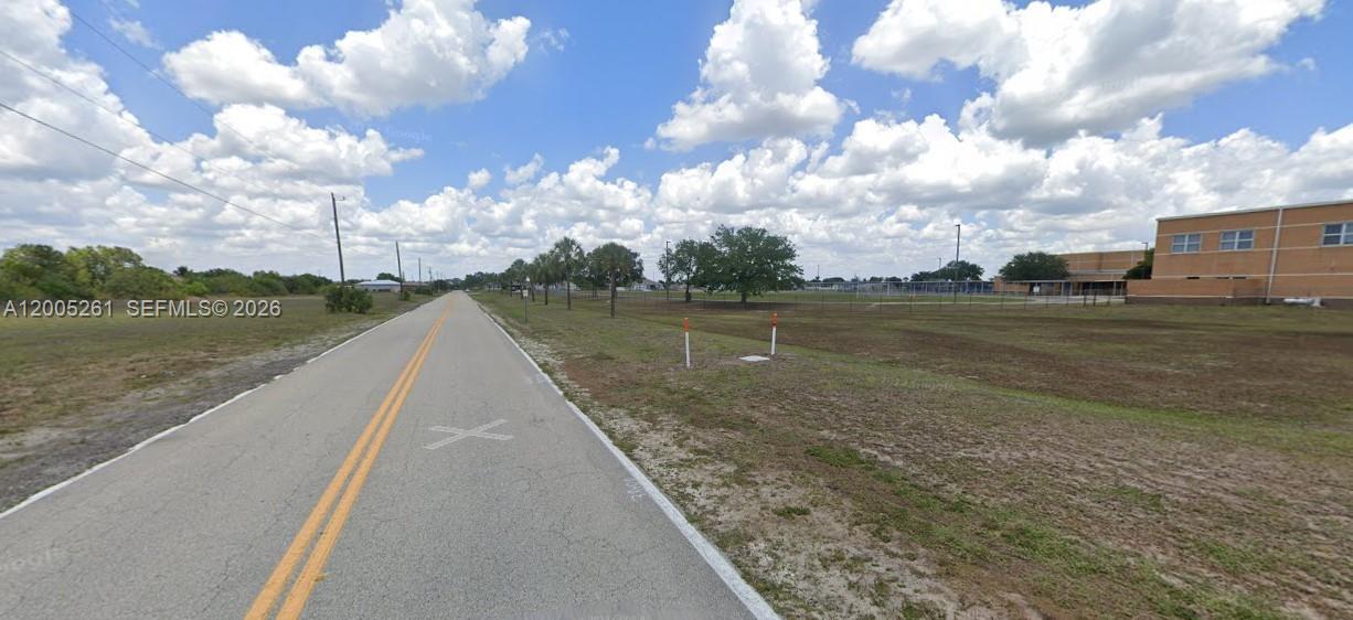A paved road runs alongside a large, open grassy field with a building in the distance — 1702 NE 10th PL, Cape Coral FL 33909, CAPE CORAL, FL