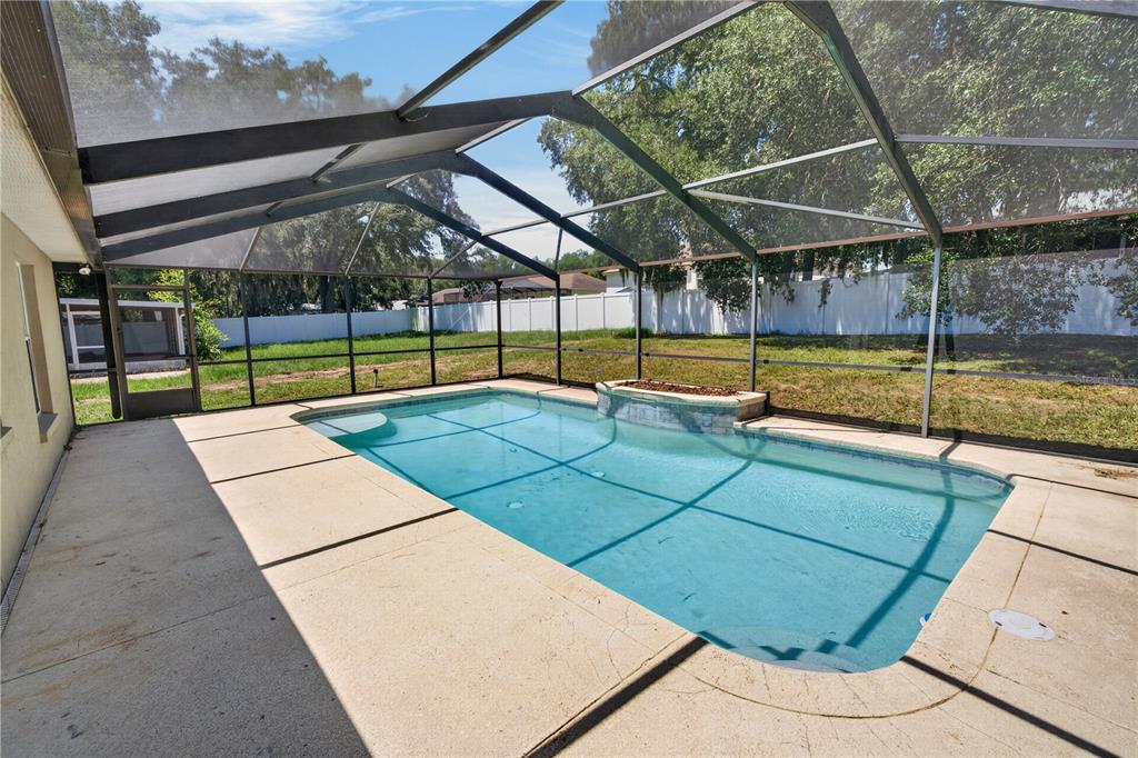 A rectangular swimming pool with a raised stone water feature inside a screened-in patio enclosure — 6035 HILLSIDE HEIGHTS DRIVE, LAKELAND, FL