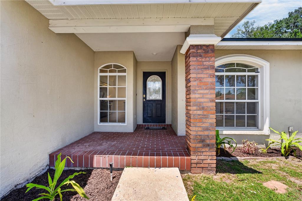 A brick-floored front porch features a dark door and a brick support column — 6035 HILLSIDE HEIGHTS DRIVE, LAKELAND, FL