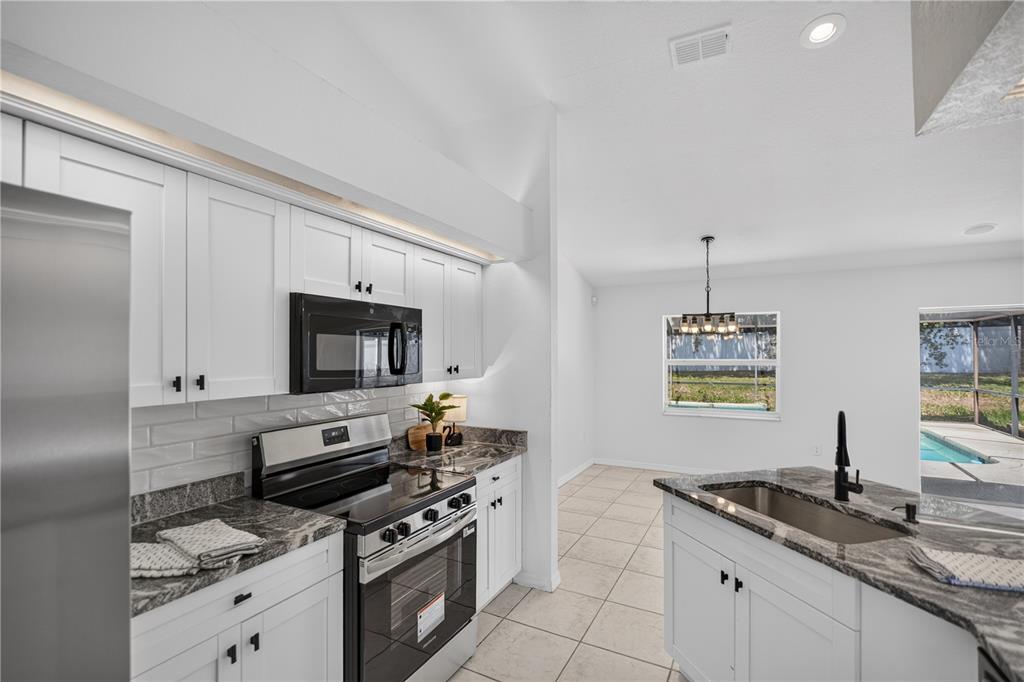 A kitchen with white cabinets, granite countertops, stainless steel appliances, and a view of a pool — 6035 HILLSIDE HEIGHTS DRIVE, LAKELAND, FL