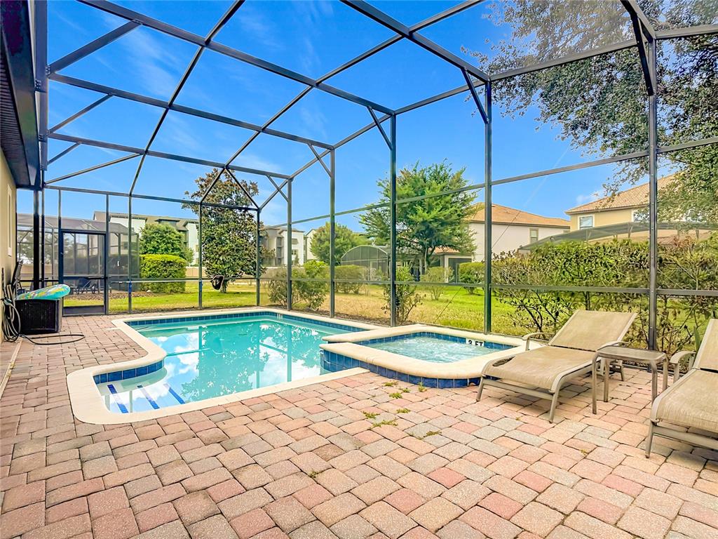 A screened-in patio features a swimming pool, a spa, and lounge chairs on pavers — 1442 MOON VALLEY DRIVE, DAVENPORT, FL