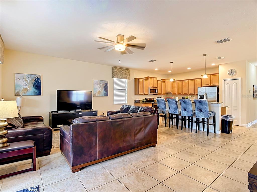 An open-concept living room features a leather sofa, a television, and a kitchen with bar seating — 1442 MOON VALLEY DRIVE, DAVENPORT, FL