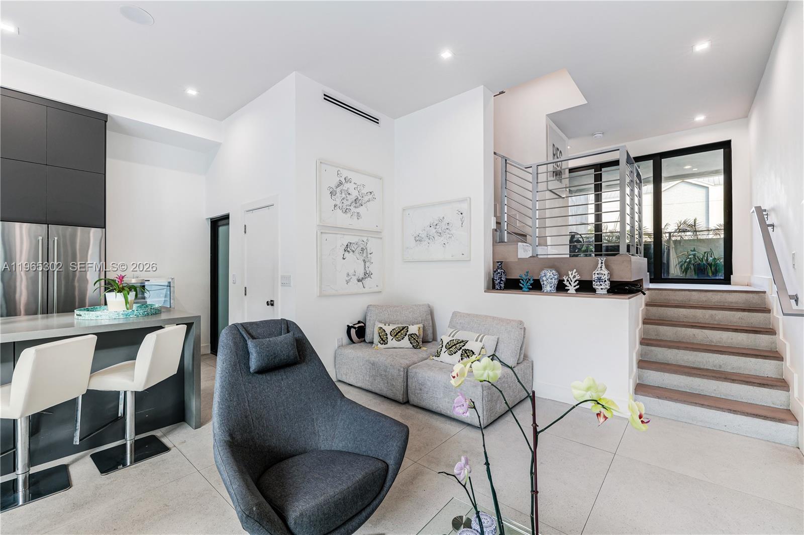 A modern living area features a kitchen island, gray armchairs, and a staircase with railings — 640 Fernwood Rd, Key Biscayne FL 33149, KEY BISCAYNE, FL