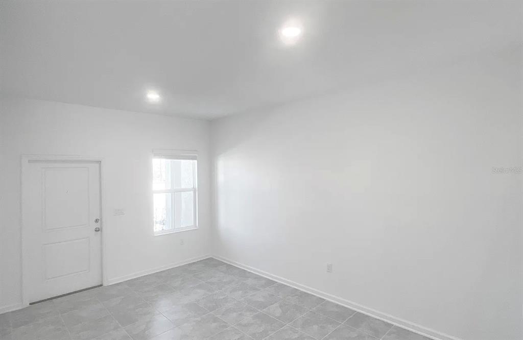 An empty room with white walls, recessed lighting, a single window, and gray tiled flooring — 2562 SKYLINE LOOP, KISSIMMEE, FL