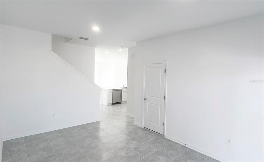 A room with gray tile flooring, white walls, a closed door, and a staircase — 2562 SKYLINE LOOP, KISSIMMEE, FL