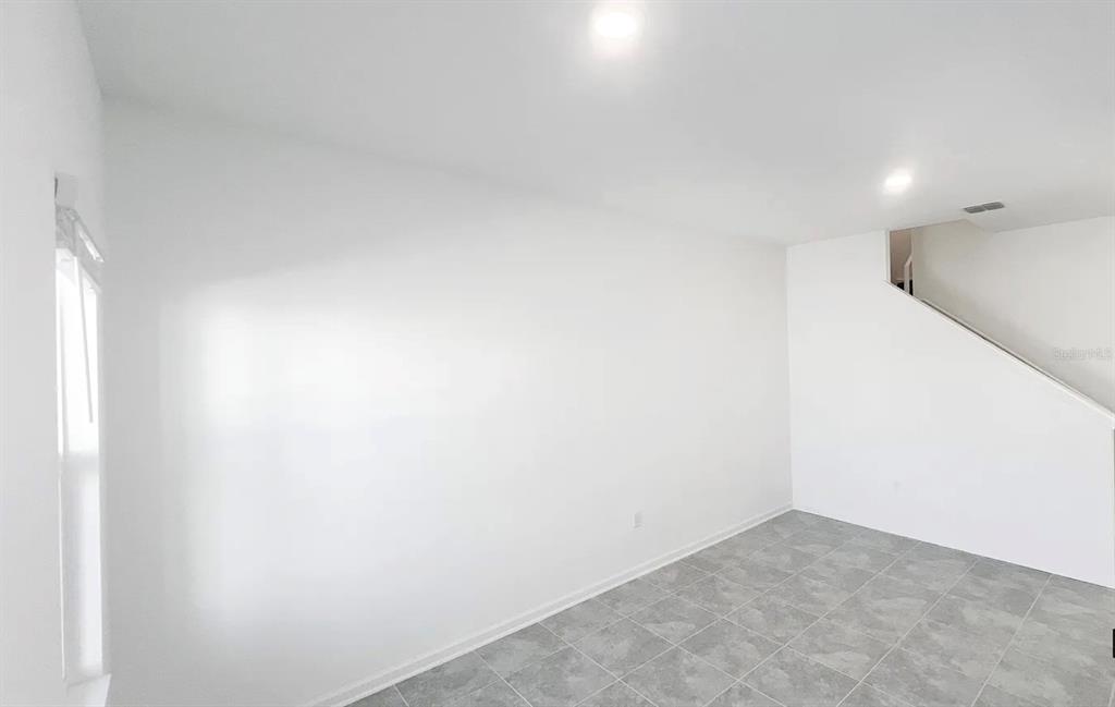 An empty room with white walls, gray tile flooring, and a staircase on the right — 2562 SKYLINE LOOP, KISSIMMEE, FL