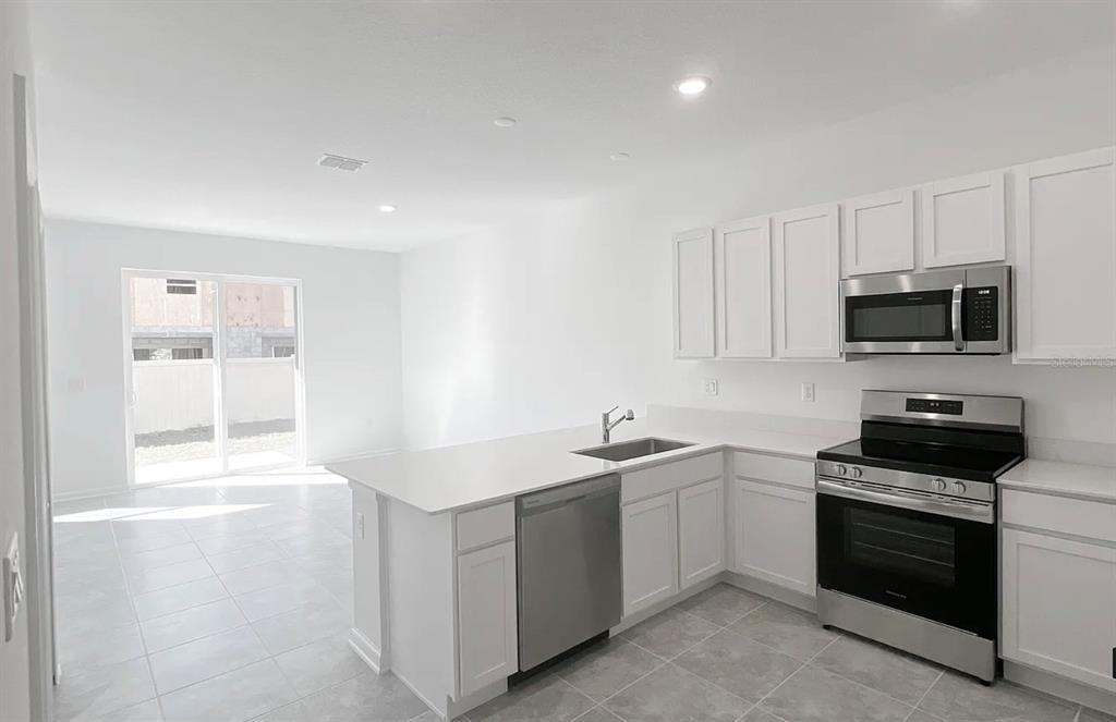 A modern kitchen with white cabinets, stainless steel appliances, and tile flooring — 2562 SKYLINE LOOP, KISSIMMEE, FL