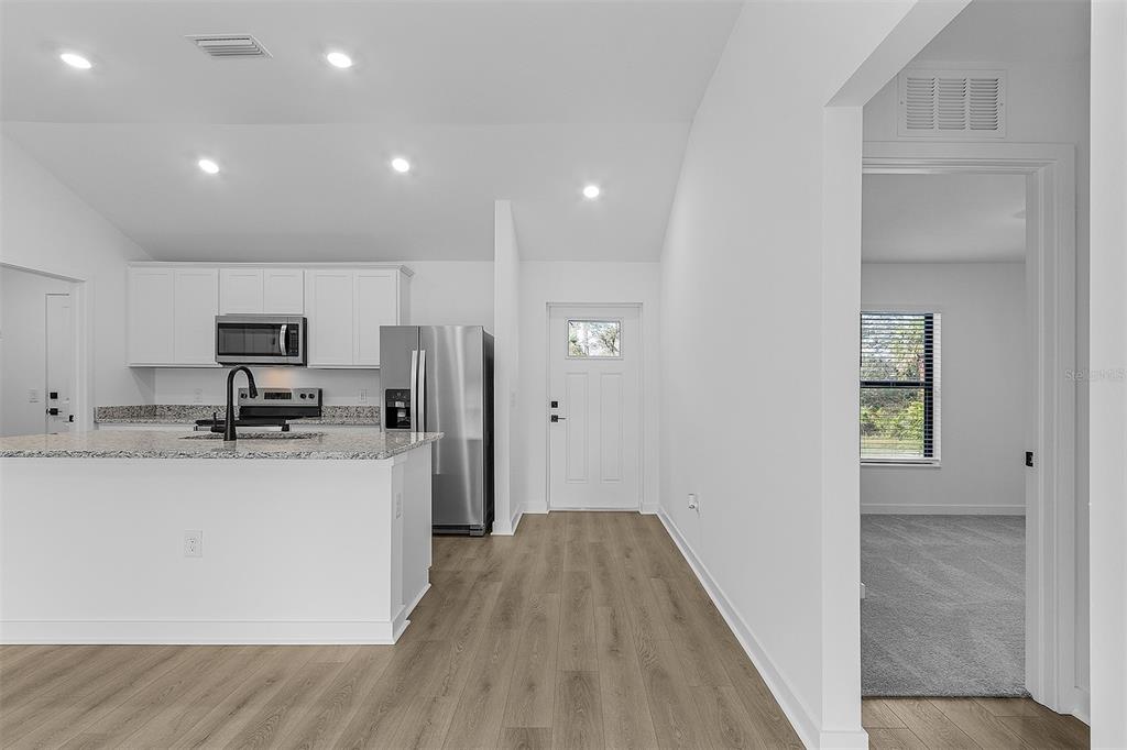 A kitchen with white cabinets and granite countertops overlooks a living area with wood flooring — 2843 SNUG STREET, NORTH PORT, FL