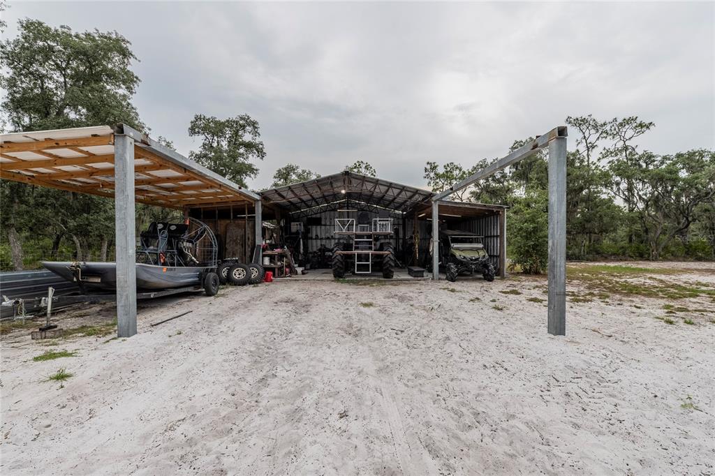 A metal-roofed pole barn with an airboat, tractor, and UTV parked under the structure — 2941 RAWLS ROAD, LAKE WALES, FL