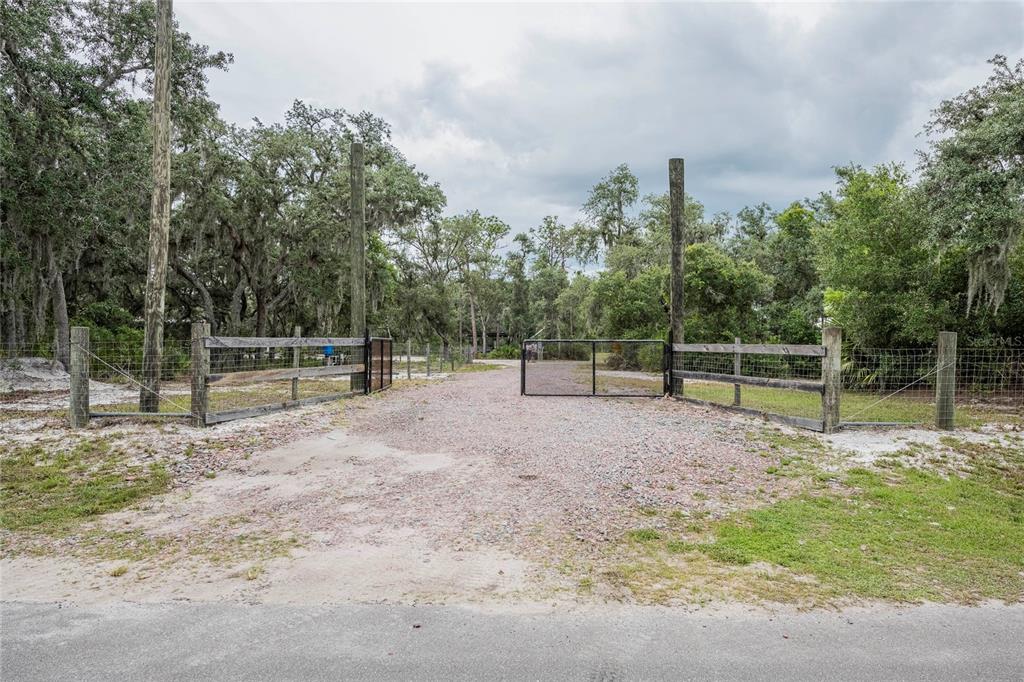 A gravel driveway leads through a metal gate into a wooded, fenced property — 2941 RAWLS ROAD, LAKE WALES, FL