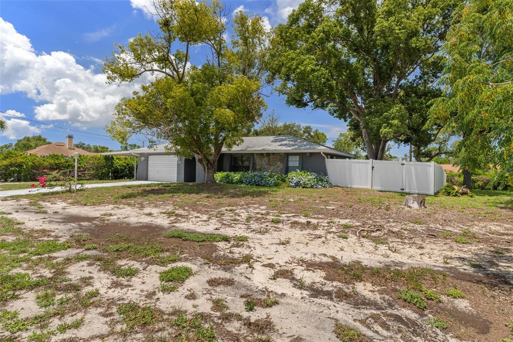 A single-story house with a garage and white fence sits on a sandy lot — 6480 INDIAN ROCK COURT, SPRING HILL, FL