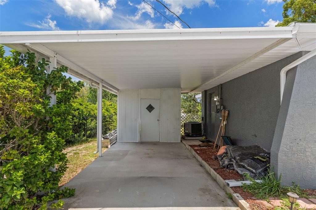A concrete carport features a white metal enclosure with a door and a gray exterior wall — 6480 INDIAN ROCK COURT, SPRING HILL, FL