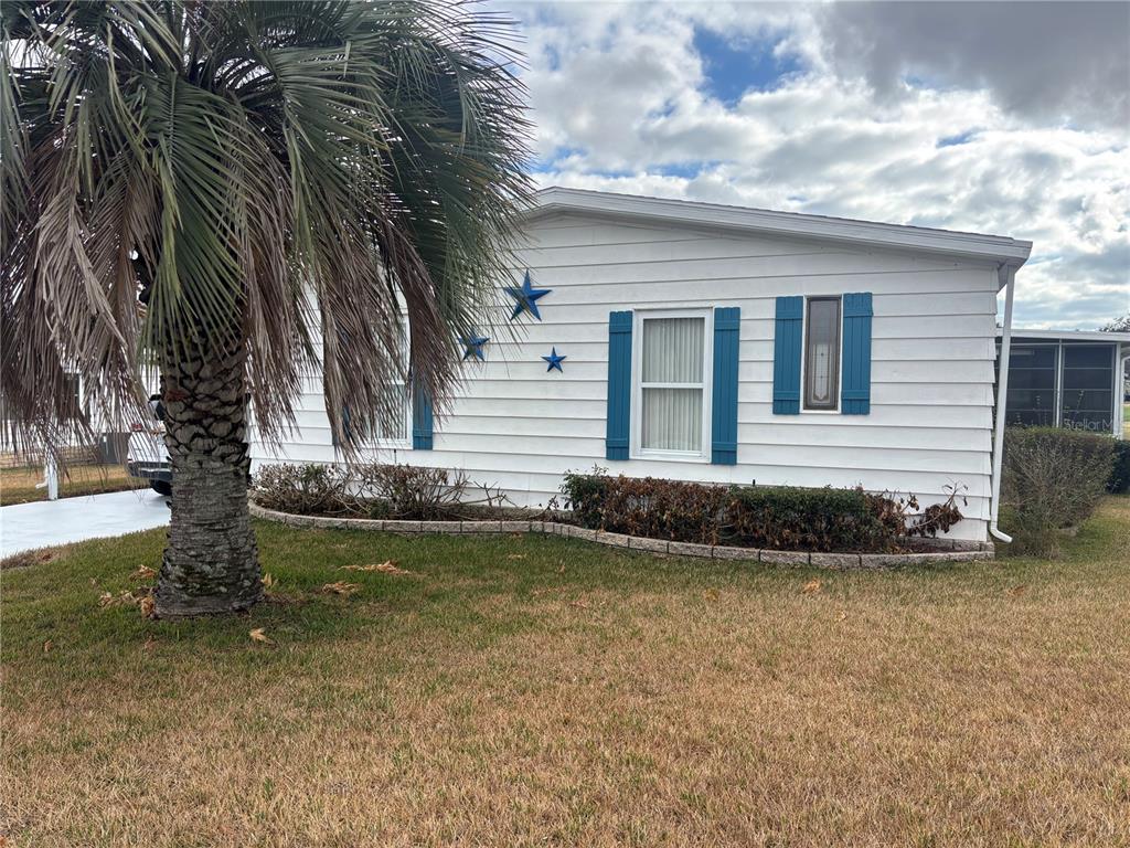 A white mobile home with blue shutters and decorative stars sits behind a palm tree — 3746 PARWAY ROAD UNIT 1349, ZELLWOOD, FL