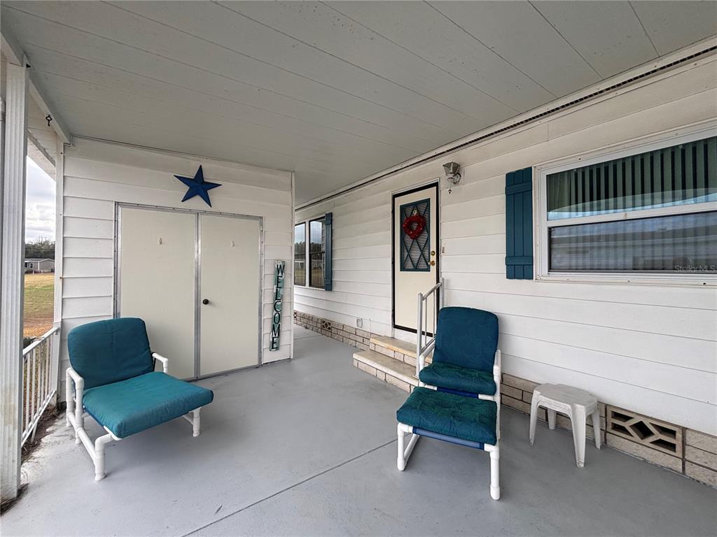 A covered porch features white siding, two blue chairs, a storage closet, and a door — 3746 PARWAY ROAD UNIT 1349, ZELLWOOD, FL