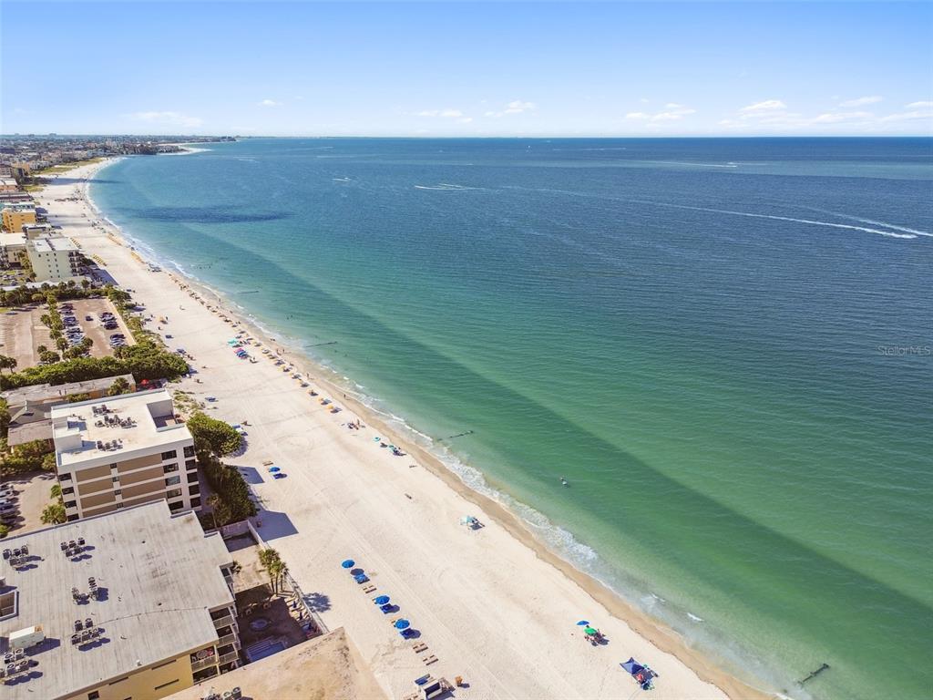 An aerial view of a sandy beach with ocean waves and nearby multi-story buildings — 223 148TH AVENUE E, MADEIRA BEACH, FL