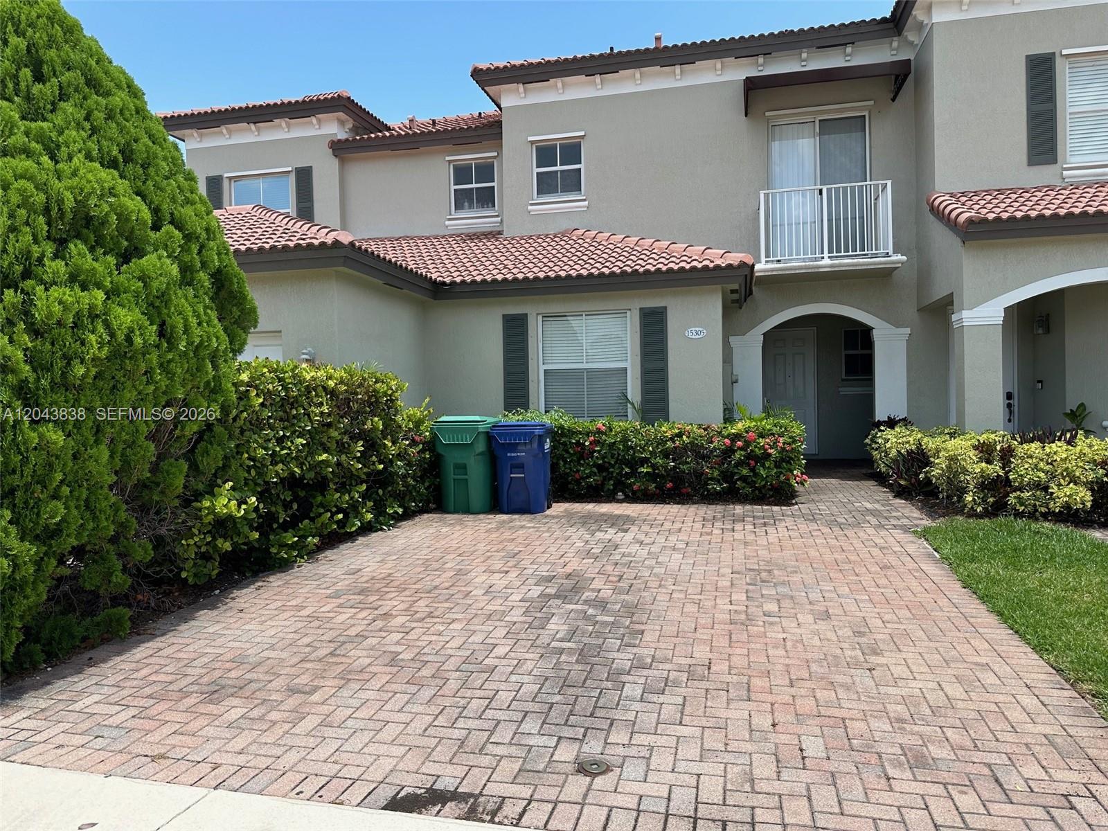 A two-story townhouse exterior features a brick paver driveway, green landscaping, and two trash bins — 15305 SW 89th Ter # 0, Miami FL 33196, MIAMI, FL