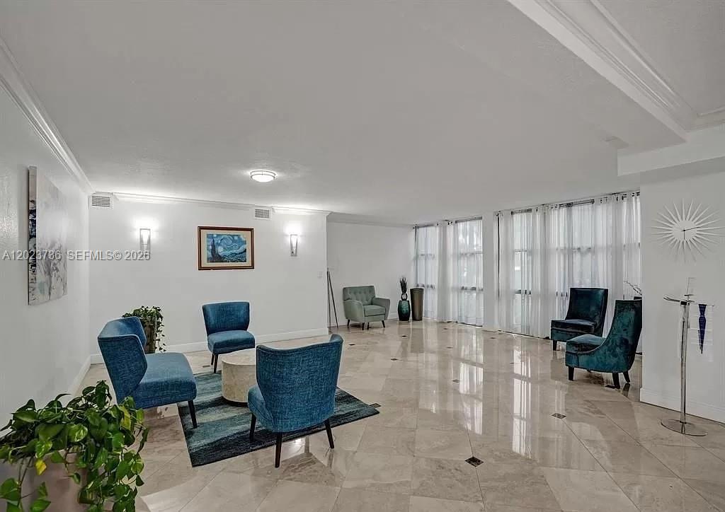 A spacious living room features light tile flooring, blue armchairs, and floor-to-ceiling window curtains — 800 Parkview Dr # 430, Hallandale Beach FL 33009, HALLANDALE BEACH, FL