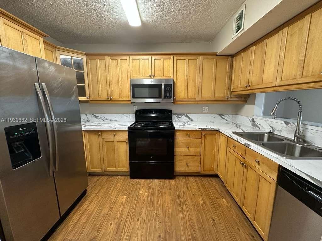 A kitchen features light wood cabinets, stainless steel appliances, and white marble-patterned countertops — 3400 Foxcroft Rd # 115, Miramar FL 33025, MIRAMAR, FL