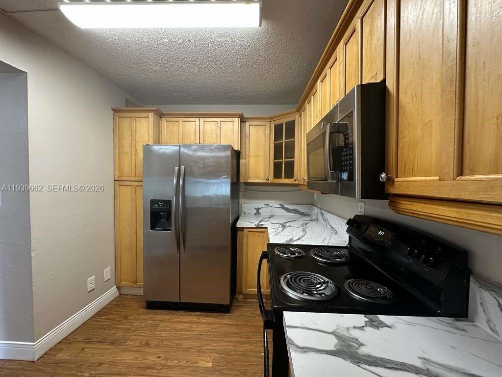 A kitchen features light wood cabinets, stainless steel appliances, and white marble-patterned countertops — 3400 Foxcroft Rd # 115, Miramar FL 33025, MIRAMAR, FL