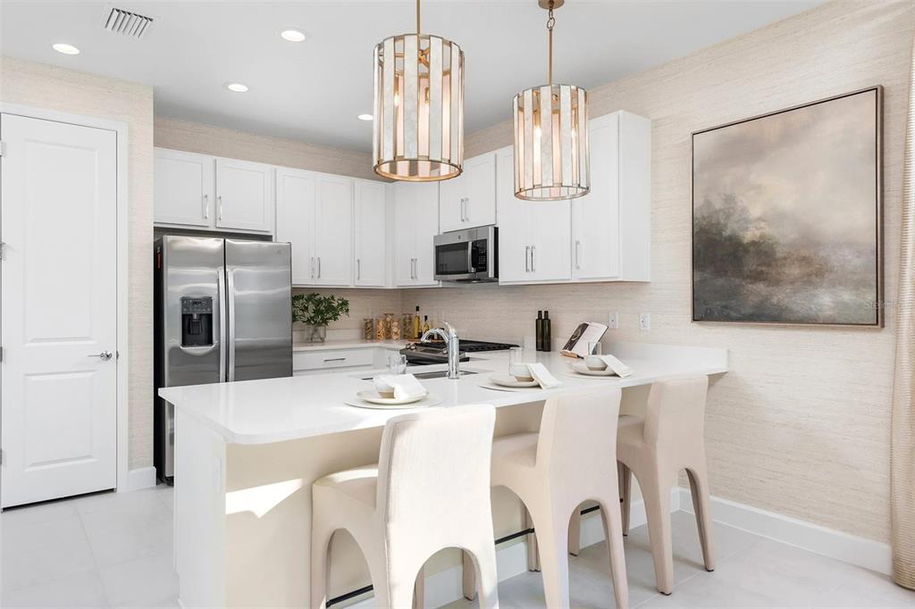 A modern kitchen features white cabinetry, stainless steel appliances, a quartz island, and pendant lighting — 3380 MALTA AVENUE, WESLEY CHAPEL, FL