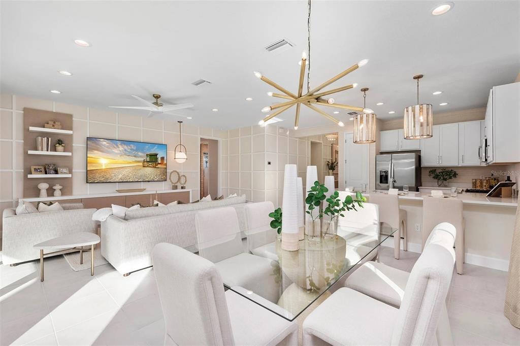 An open-concept living and dining area features a modern chandelier, glass table, and white cabinetry — 3380 MALTA AVENUE, WESLEY CHAPEL, FL