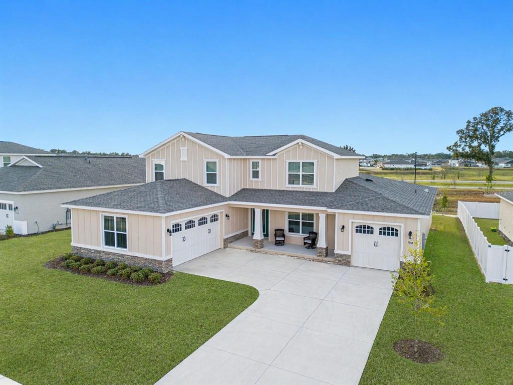 A two-story house with tan vertical siding, stone accents, and a three-car garage — 7610 SW 60TH STREET, OCALA, FL