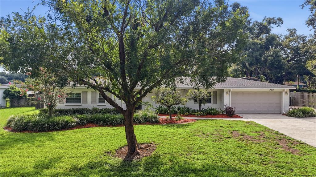 A single-story white brick house features a two-car garage and a large front yard tree — 2103 RAMBLEWOOD LANE, BRANDON, FL