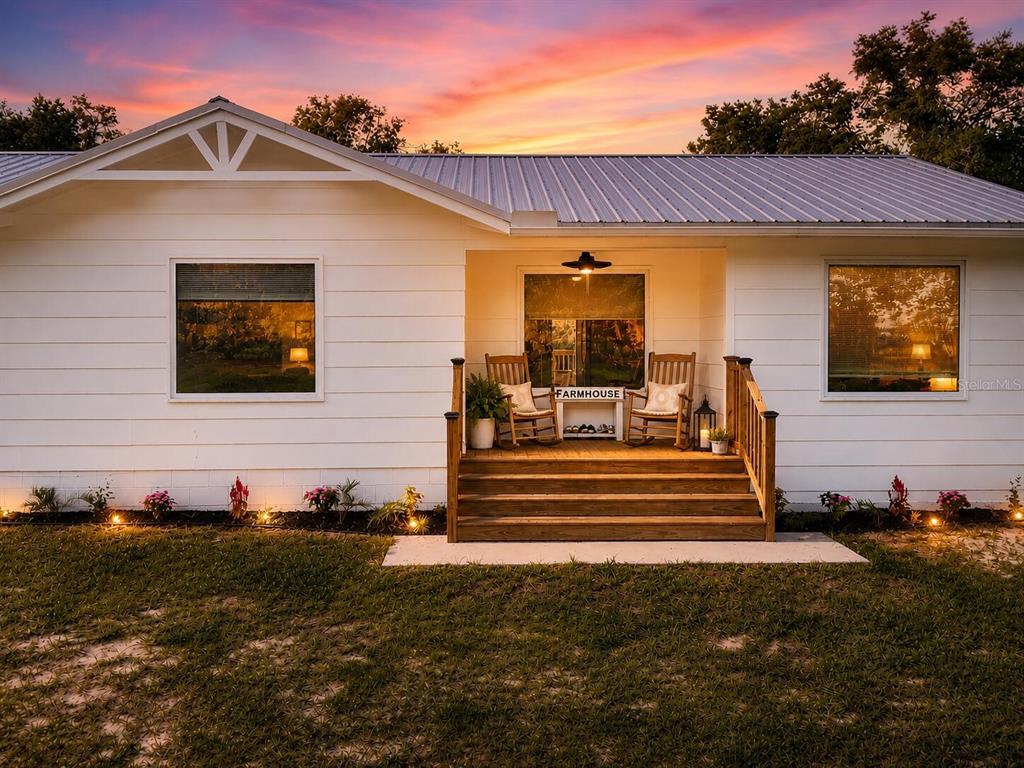 The exterior of a white house at dusk features a wooden porch and patio chairs — 6320 SE 91ST TRAIL, TRENTON, FL