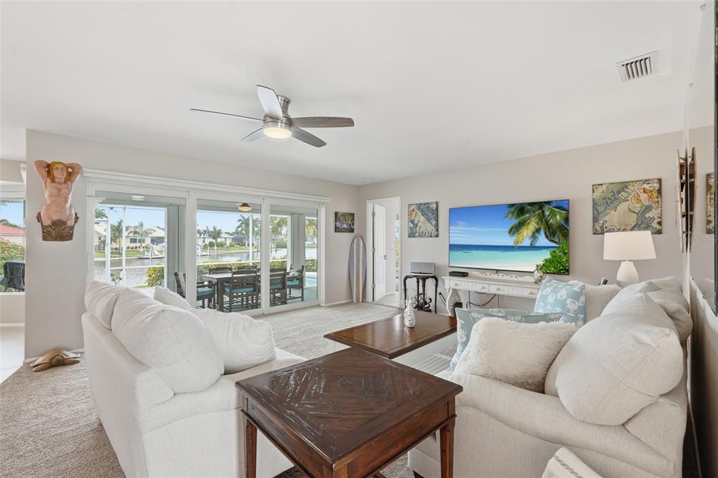 A living room with white sofas, a television, and sliding glass doors overlooking a canal — 3433 NIGHTHAWK COURT, PUNTA GORDA, FL