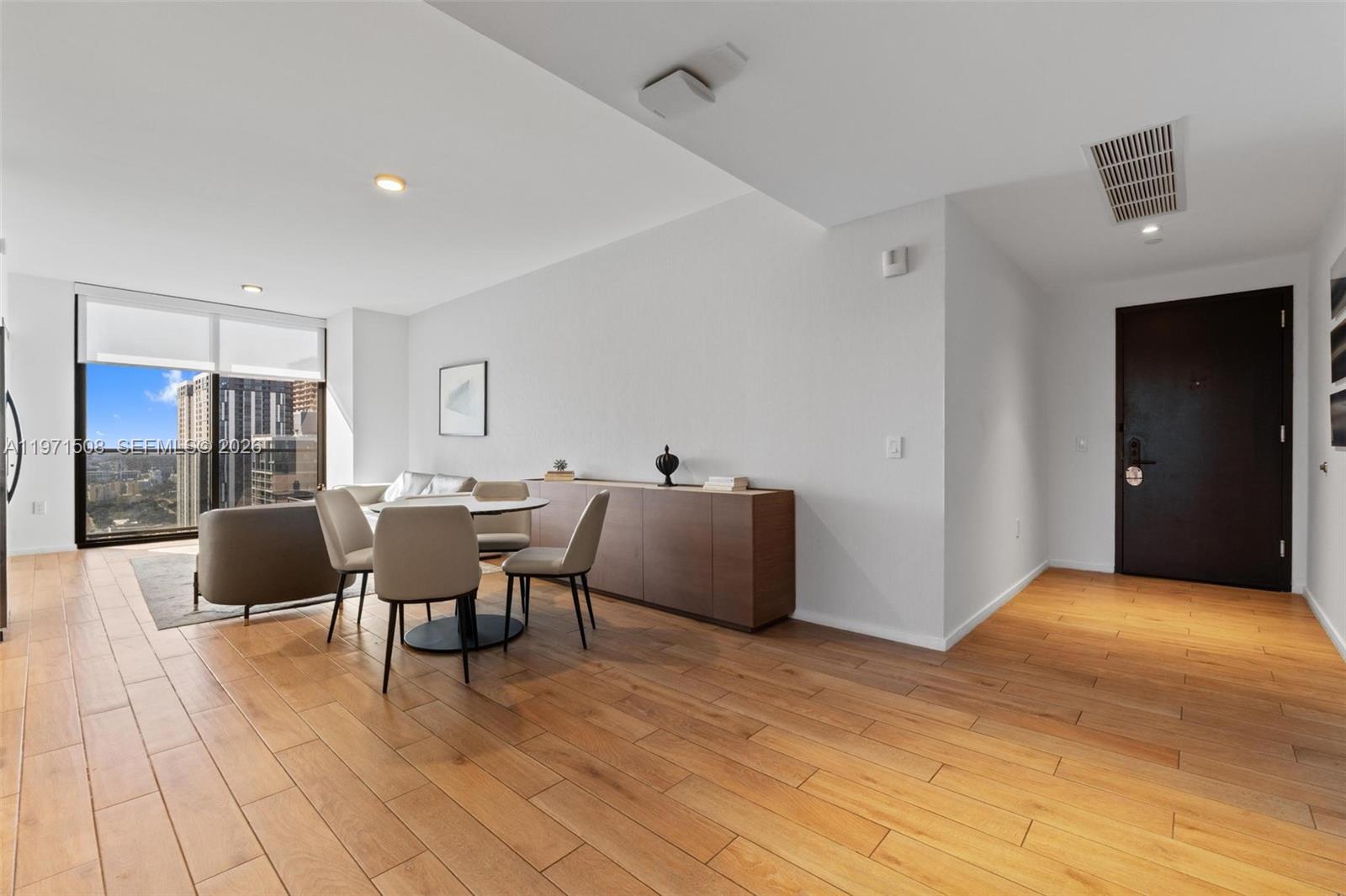 A modern living and dining area features light wood flooring, a dark door, and floor-to-ceiling windows — 398 NE 5th St # 3218, Miami FL 33132, MIAMI, FL