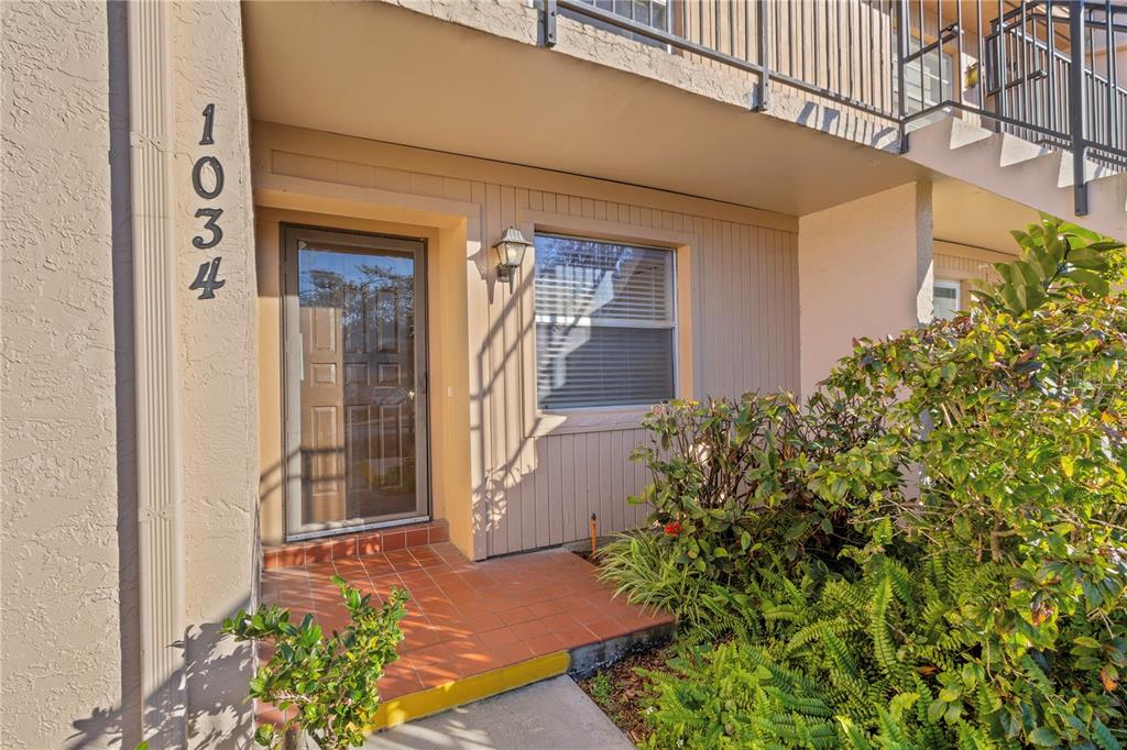 The exterior of a ground-floor apartment entrance features a tiled porch and a screen door — 1034 BOWSPRIT LANE, HOLIDAY, FL