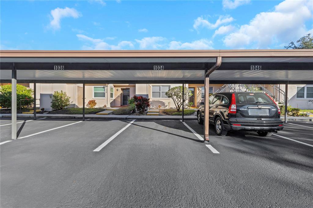 A covered parking area with numbered spaces sits in front of a multi-unit residential building — 1034 BOWSPRIT LANE, HOLIDAY, FL