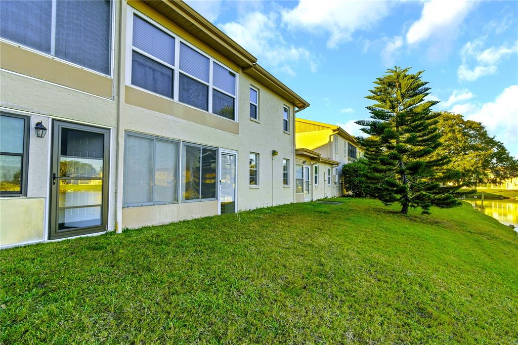 The exterior of a multi-story residential building features a grassy lawn and a large pine tree — 1034 BOWSPRIT LANE, HOLIDAY, FL