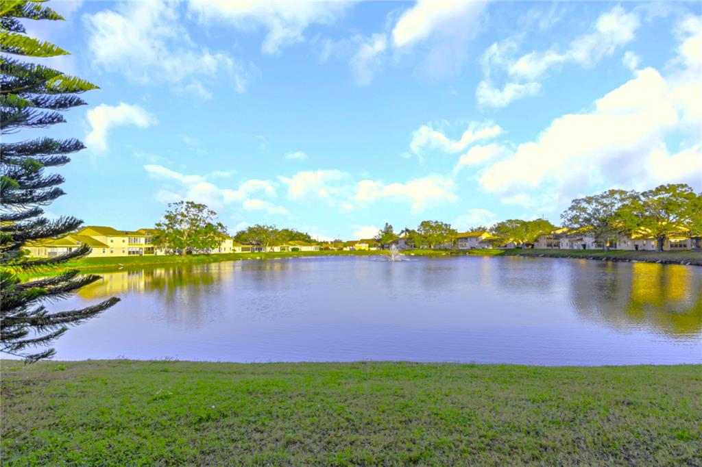 A view of a pond with a fountain surrounded by residential buildings and green grass — 1034 BOWSPRIT LANE, HOLIDAY, FL