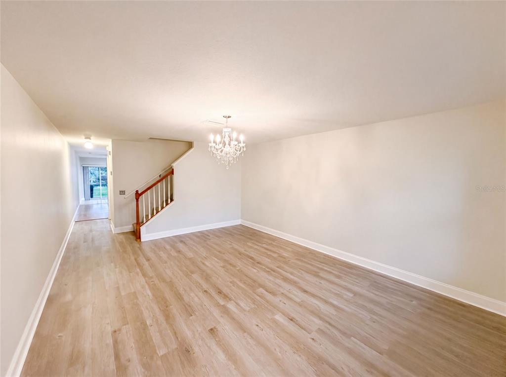 An empty living room features light wood-look flooring, white walls, and a central crystal chandelier — 112 COQUINA BAY DRIVE, ST PETERSBURG, FL
