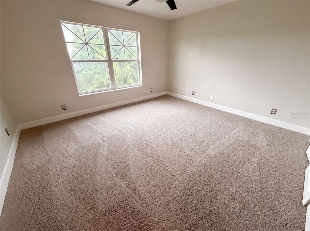 An empty bedroom features beige walls, tan carpeting, and a large window — 112 COQUINA BAY DRIVE, ST PETERSBURG, FL