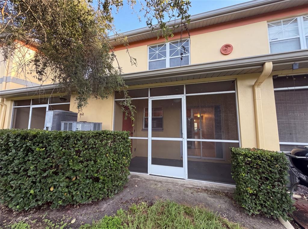 A screened-in patio sits between two hedges in front of a two-story yellow townhouse — 112 COQUINA BAY DRIVE, ST PETERSBURG, FL