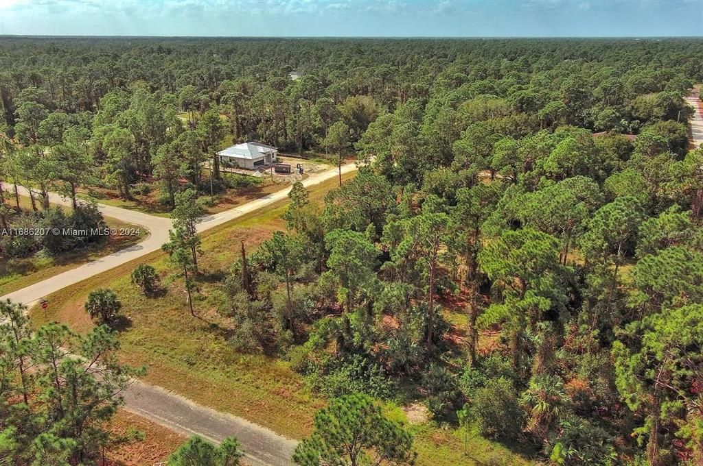 An aerial view shows a house under construction surrounded by dense pine forest and roads — 158 NAGEL AVENUE S, LEHIGH ACRES, FL
