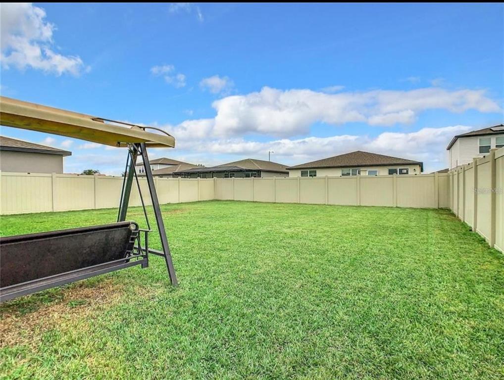A grassy backyard features a metal swing set and is enclosed by a tall vinyl fence — 1210 ZAMBRANA COURT, WINTER HAVEN, FL