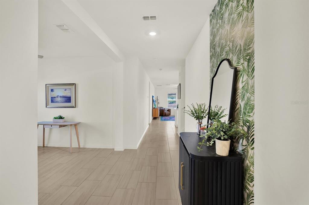 A hallway with light tile flooring leads past a wallpapered accent wall to a living area — 11307 LINDEN DEPOT ROAD, SAN ANTONIO, FL