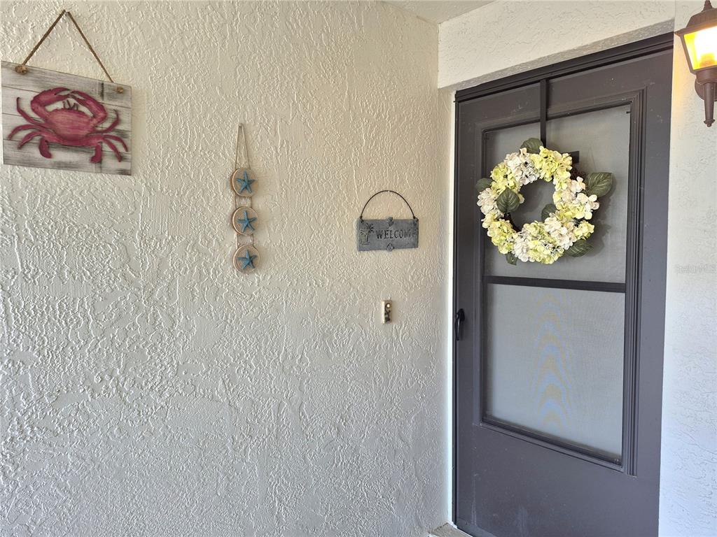 A front door with a wreath and coastal-themed wall decor on a textured exterior wall — 107 WINDWARD PLACE UNIT 107, OLDSMAR, FL