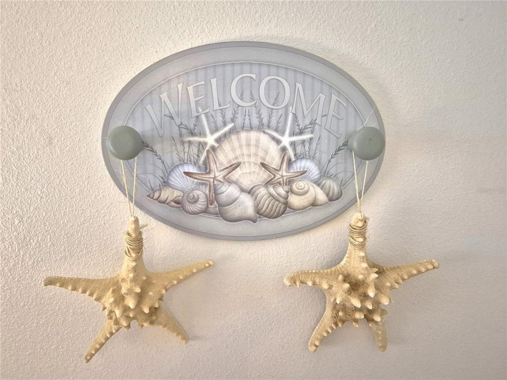 A coastal-themed wall-mounted welcome sign features two hooks holding decorative starfish ornaments — 107 WINDWARD PLACE UNIT 107, OLDSMAR, FL