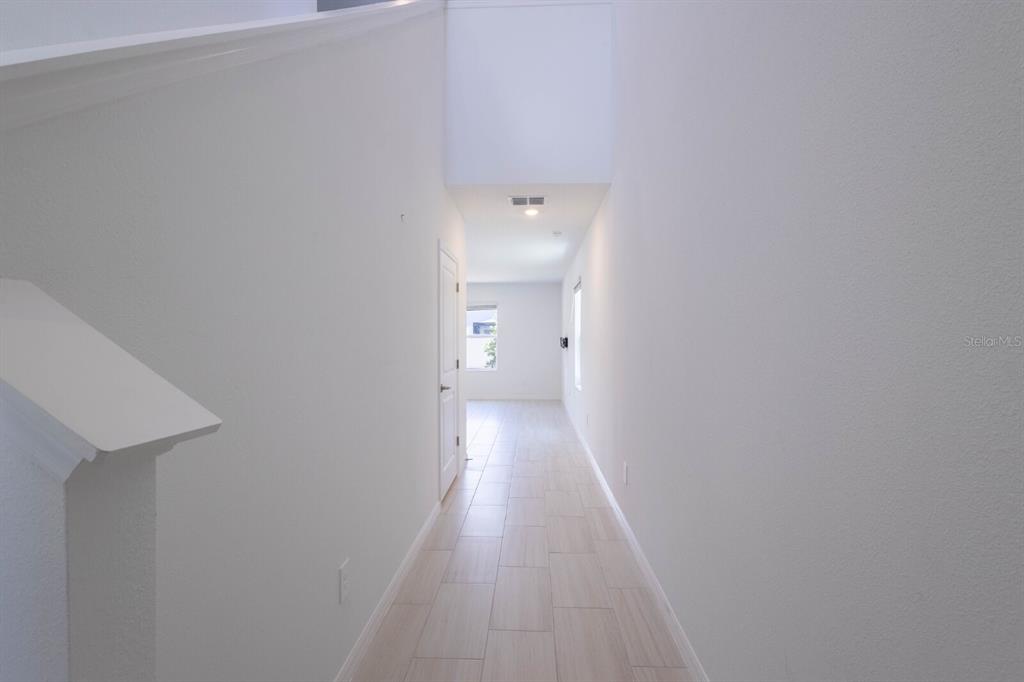 A narrow hallway with light-colored tile flooring leads toward a bright room with windows — 17534 SHIREWOOD WAY, LAND O LAKES, FL