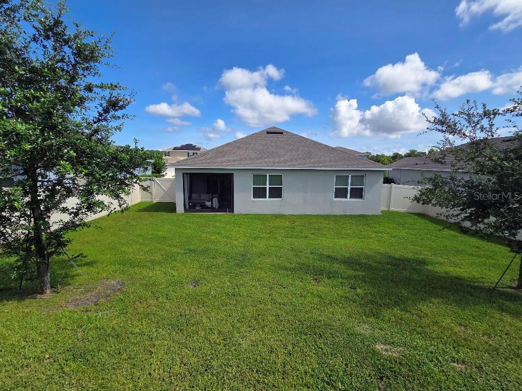 The rear exterior of a single-story house features a screened patio and a grassy yard — 5268 GREENHEART AVENUE, MOUNT DORA, FL