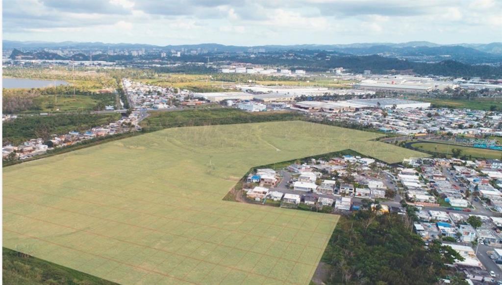 An aerial view shows a large, undeveloped grassy lot adjacent to a residential neighborhood — 28 ACRES VACANT RESIDENTIAL LAND – CATAÑO, PUERTO, CATANO, PR
